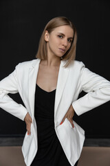 beautiful fashion caucasian woman in a black dress and white jacket in the studio on a black background looking at the camera