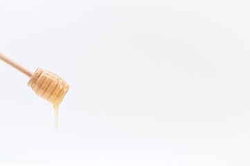 honey dripping from a wooden dipper against white background