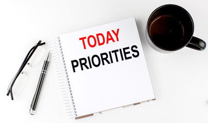 Coffee,glasses,pen and notebook written with TODAY PRIORITIES , on white background.