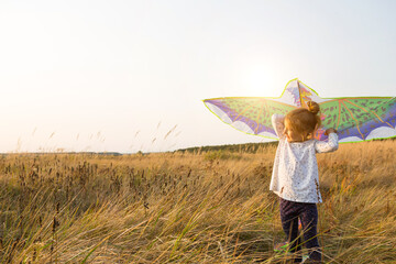 A girl runs into a field with a kite, learns to launch it. Outdoor entertainment in summer, nature and fresh air. Childhood, freedom and carelessness. A child with wings is a dream and a hope.