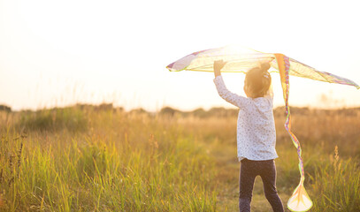 A girl runs into a field with a kite, learns to launch it. Outdoor entertainment in summer, nature and fresh air. Childhood, freedom and carelessness. A child with wings is a dream and a hope.