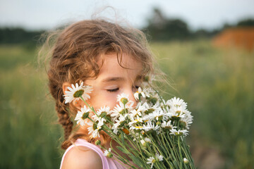 Portrait cute child girl with a bouquet of chamomile in summer on a green natural background. Happy child, hidden face, no face, covered with flowers. Copy space. Authenticity, rural life, eco-friendl