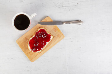 coffee mug, a piece of white bread with strawberry jam and a silver knife, view from above