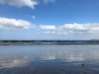 Seascape of sandy ocean coast at low tide. Reflection of white clouds and blue sky in a wet sand.