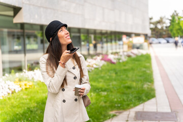 Businesswoman outside the office with a coffee in her hand and sending a voice note with the phone