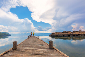Wooden pier and cloudscape with a couple at the end of the dock in the bay known as bay of bones in Lake Ohrid, Macedonia.