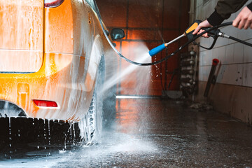 Fototapeta na wymiar Washing a yellow car at a contactless self-service car wash. Washing a sedan car with foam and high-pressure water.