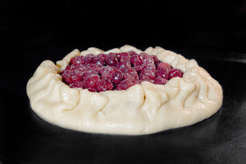 Uncooked galette, open pie with cherry baking on tray in electric oven. Homemade bakery, food, cooking, pastry and semi-finished products concept