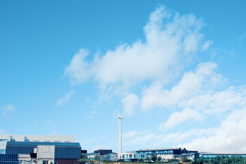 Wind turbine in the middle of industrial estate as a source of renewable energy on blue sky...