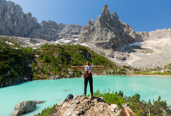 A woman standing with open arms by the turquoise lake. Location: Europe, Italy, Lake Sorapis