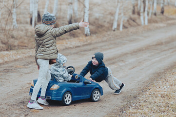 Three happy children playing with old toy car in countryside, outdoors.