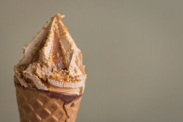 Ice cream cone on grey wall background with copy space. Caramel ice cream in waffle. Creamy dessert. Refreshing cold dessert. Melting ice cream. Summer lifestyles. Sweet food concept. 