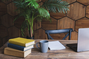 Wooden desk with a laptop, a mug and a stack of books. Cozy workplace. Teacher's office