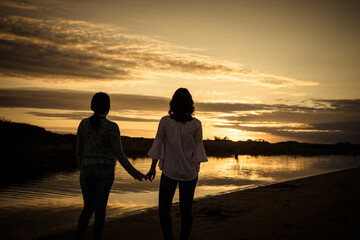 couple of women holding hands watching sunset golden hour with lake view