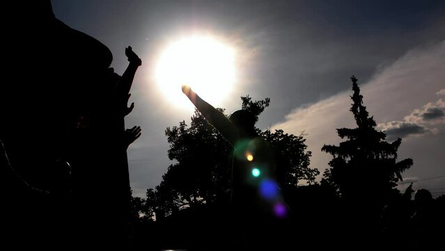 Hare Krishnas dance in public with religious chants during sunset. Silhouettes of happy people dancing religious dances slow motion. A backlit crowd of people dances on a sunny summer evening.