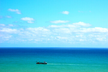 Fototapeta na wymiar Heavenly view of the Adriatic Sea in Ortona with intensifying blue color reaching up to the horizon and a white-black boat lightly skimming its surface