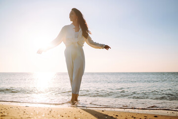 Young woman walks along the seashore. The girl looks at the magical sunrise. Travel, weekend, relax...