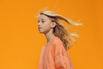 a beautiful, sweet girl, blonde, of school age, stands on an orange background in bright clothes...