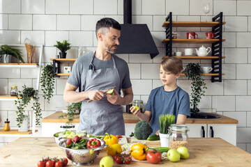 Handsome father and his teenager son spending quality time together. Men doing chores, cooking healthy vegetable salad, tasty food in the kitchen at home