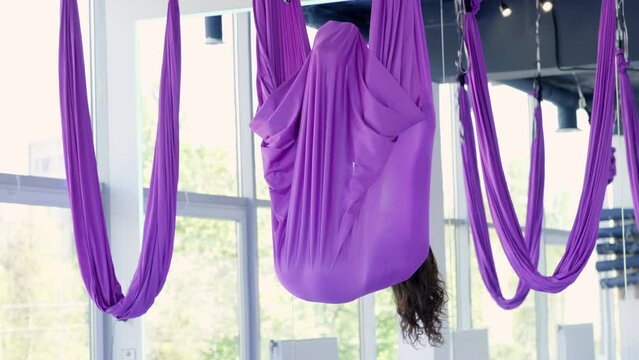 Young beautiful woman practicing aerial yoga stretching in purple hammock swing in fitness studio, healthy lifestyle and balance training, wellness and flexibility exercise