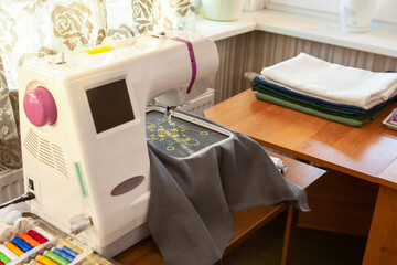 Home sewing workshop, workplace opposite the window, with a modern embroidery machine that creates...