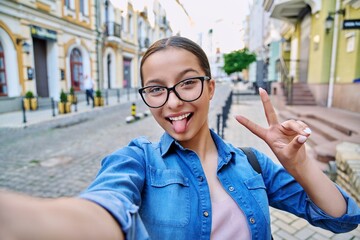 Selfie portrait of beautiful cheerful teenage girl, outdoor on city street