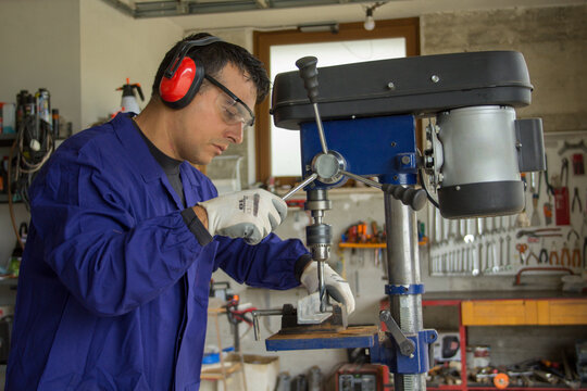 Photo of a blacksmith in his workshop while making holes with a pillar drill on an iron bar for the construction of a railing. Manual and do-it-yourself jobs