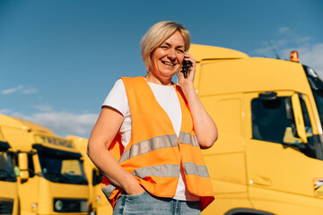 Happy middle-aged woman having a phone call in front of yellow semi-truck vehicle 
