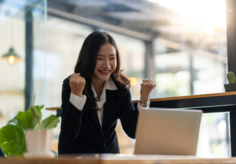 Happy young asian businesswoman sitting on her workplace in the office. Young woman working at laptop in the office