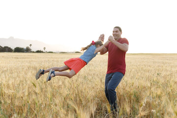 Dad spins his daughter on field , having fun at sunset. Father plays with child. Happy family and childhood concept. 