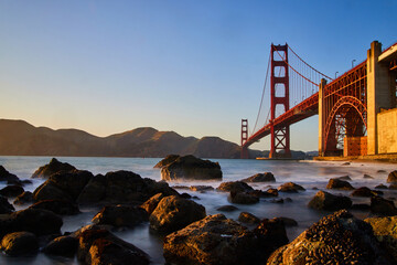 Soft waves on rocky beach by sunset at Golden Gate Bridge