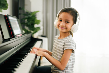 Cinematic portrait of cute asian 6 years old is enjoy playing piano of online class at home, concept of learning, art, steam, musical, homeschool, virtual, online and distance education concept.