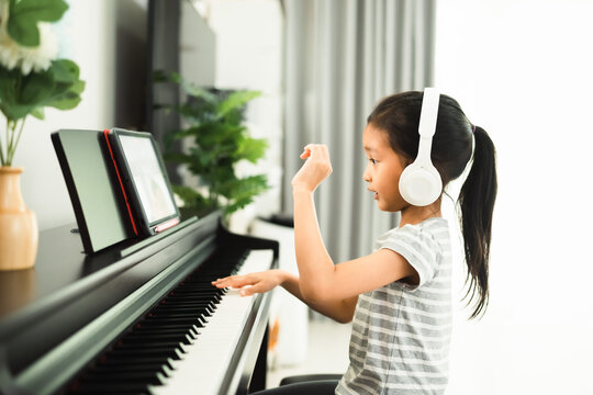 Cute asian 6 years old is enjoy playing piano of online class at home, concept of learning, art, steam, musical, mental health, homeschool, virtual, online and distance education concept.