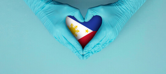 Doctors hands wearing blue surgical gloves making hear shape symbol with philippines flag