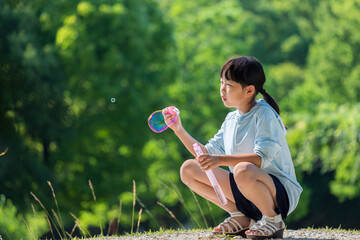 夏の公園でシャボン玉を遊んでいる小学生の女の子の様子