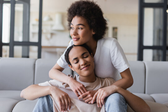 Young african american woman embracing girlfriend on couch at home