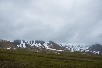 Dramatic alpine landscape with snowy mountains in gray low clouds. Bleak atmospheric scenery of...