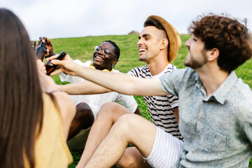 Group of multiracial friends drinking beer enjoying free day at weekend - Diverse millennial people having fun cheering with drinks relaxing on park in summer vacation - Friendship and celebration