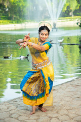 Indian woman Odissi dancer doing classical dance form outdoor at nature park. Orissi dance. art and culture of india.