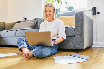 Adult woman working from home using a laptop, sitting on the living room floor