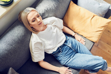 Overhead picture of relaxed adult woman resting on a sofa with eyes closed