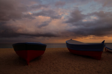 Dos barcas descansan en la arena al atardecer con nubes de tormenta sobre el mar