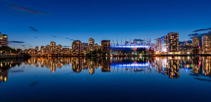 Urban city night, Vancouver marina twilight panoramic view. Skyline and buildings lights reflection on False Creek water. British Columbia, Canada. BC Place.