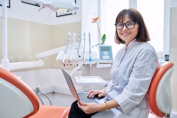 Portrait of doctor sitting in office with laptop in her hands looking at camera