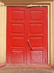 Old red double door. Cracked and peeling red paint on a wooden door. Vintage and retro style. Scarlet old-fashioned double doors. Main entrance into an abandoned house.