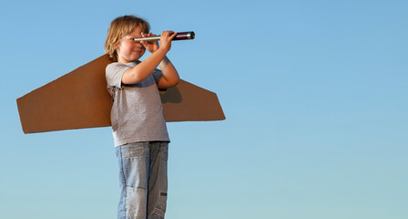 Happy boy with cardboard boxes of wings against sky looking through a telescope