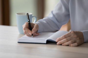 Close up middle-aged woman sit at desk write in paper planner, create important notes or meetings...