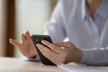 Business mobile application usage, agenda and calendar, modern wireless technology concept. Unknown older businesswoman sit at desk holding smartphone, make call, check e-mail, close up cropped image
