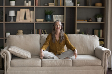 Older woman in headphones visualize while listen audio affirmations records feels serenity seated...