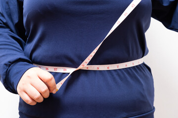 Close up shot at hand of women while use measure tape with her tummy or waist belly of chubby women that show sign of overweight. On white background with copy space for text